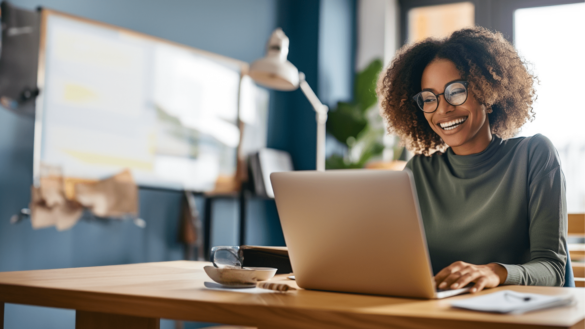 A woman smiling with curly hair working on a laptop.