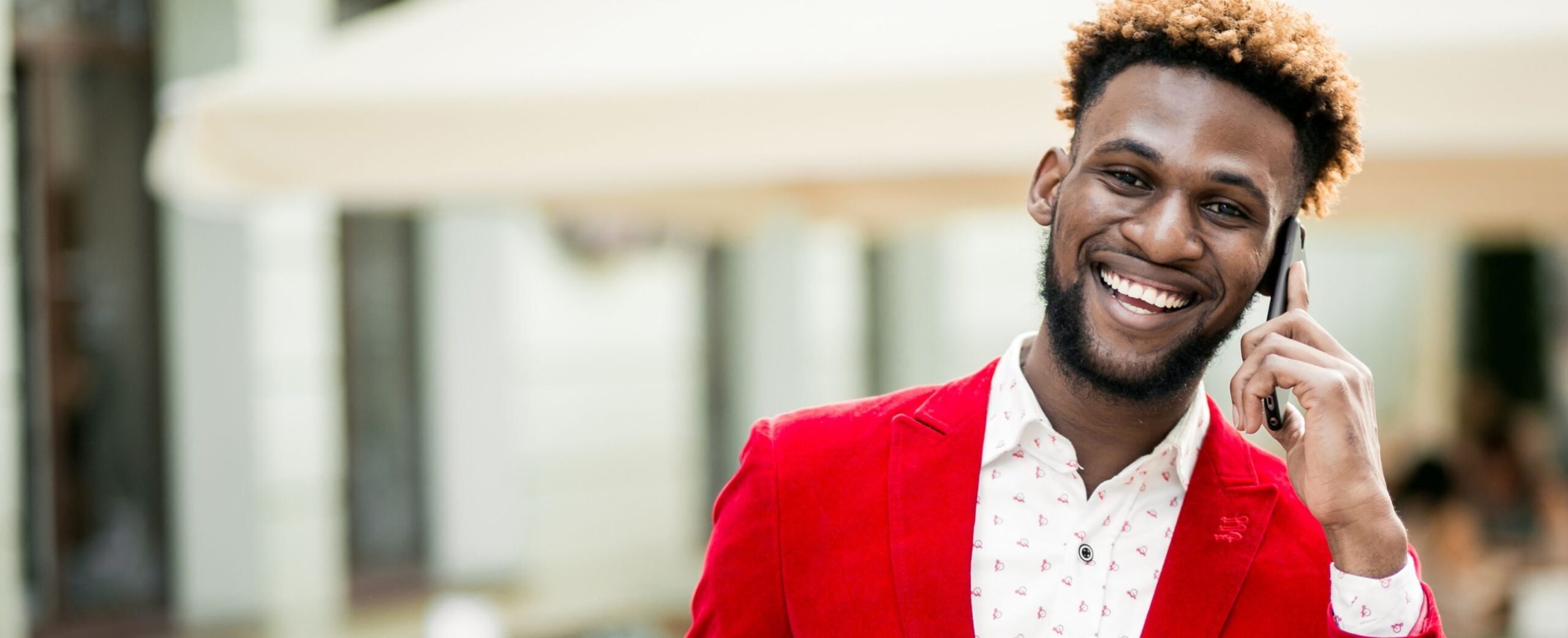 A smiling man with curly hair wearing a red blazer jacket